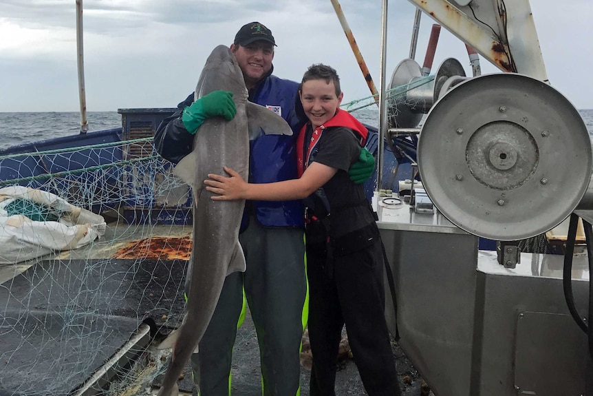 Warwick Treloggen and his son Noah pose with a shark on a fishing boat.