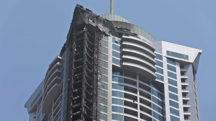 A high residential tower stands with one side completely charred.