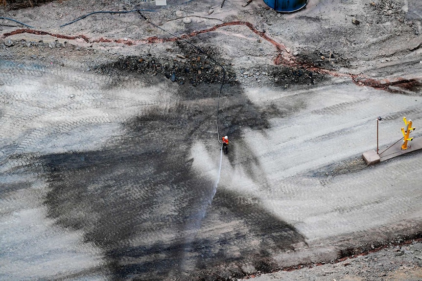 A worker hoses down the grey mine area to control dust.