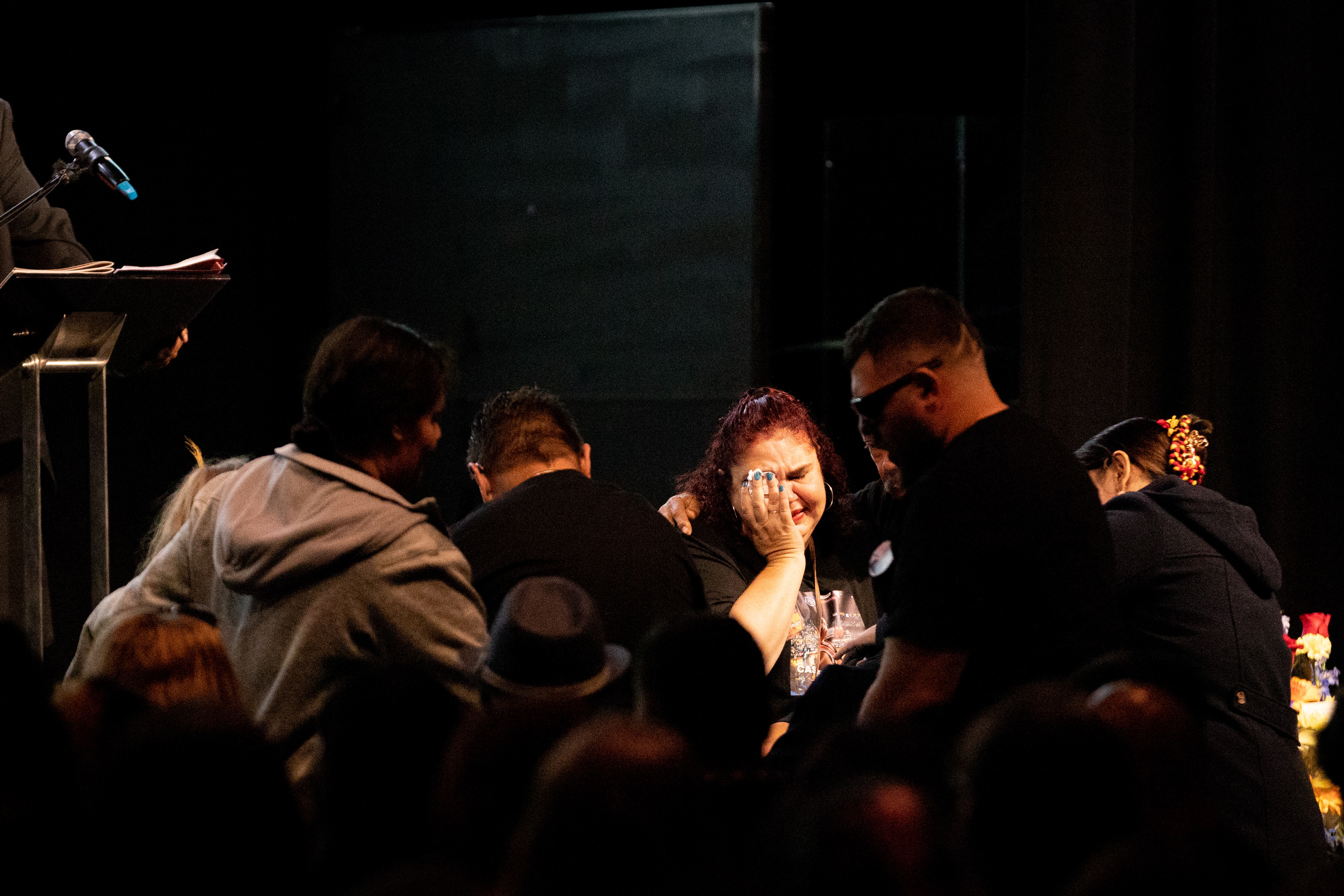 People gather at an indoor funeral service as a woman wipes tears