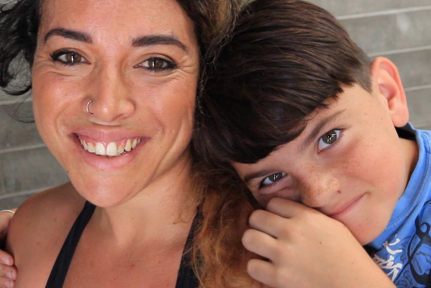 Close up on a smiling woman and a young boy who has his head on her shoulder and his arms around her.