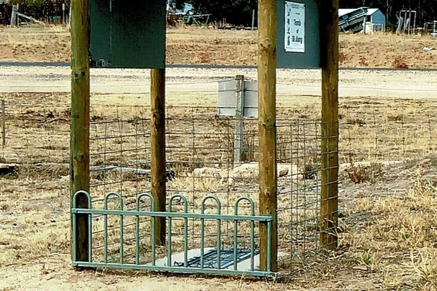 A gazebo and fence surrounding a headstone on the ground with roadworks and construction in the background.