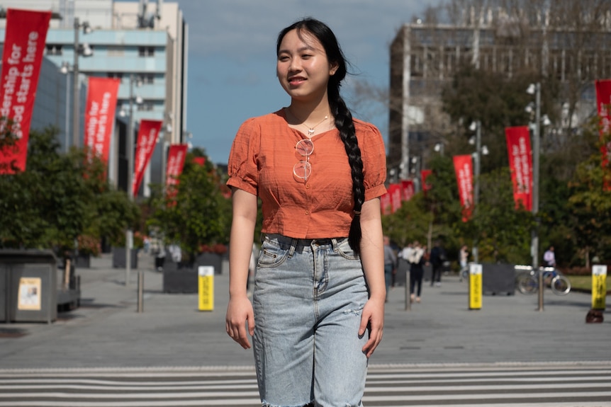 A young woman with black hair walks through a university campus.