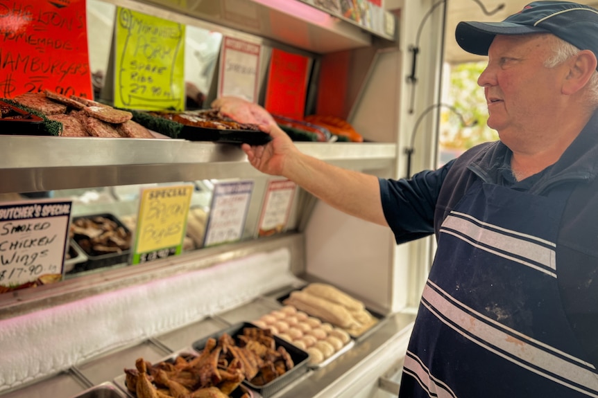 A male butcher taking packaged meat of a shelf inside a shop