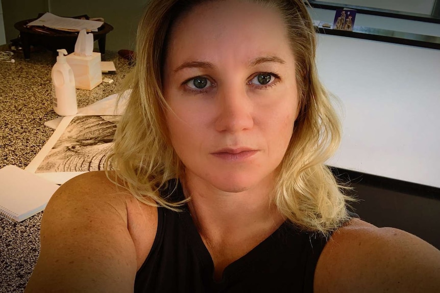 A woman with blonde hair in her home, tissues in the background on a counter top