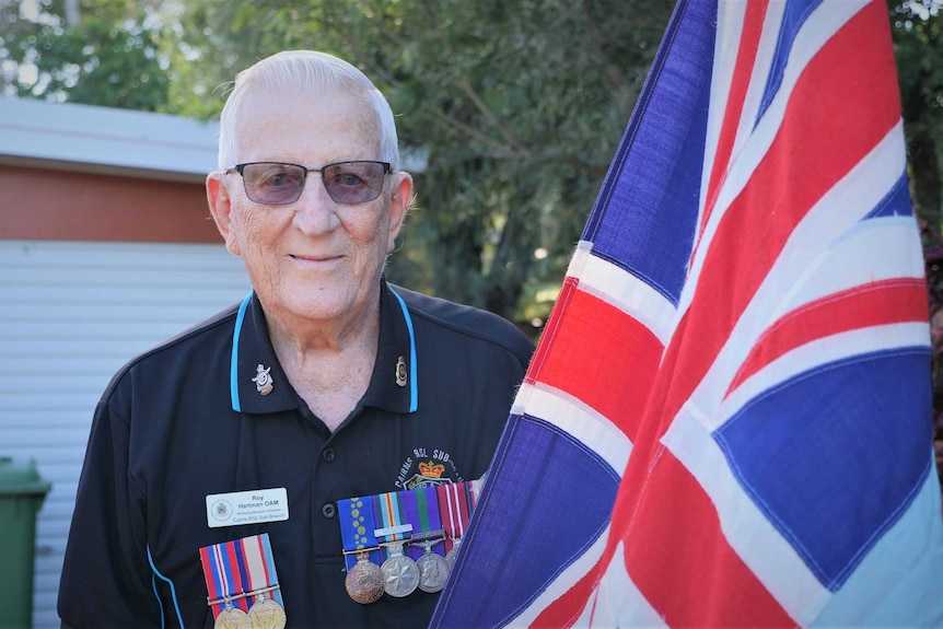 Royal Australian Air Force veteran Roy Hartman OAM stands next to a flag in his driveway in Cairns.