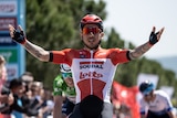 Caleb Ewan raises his arms out in front of him while riding a bike