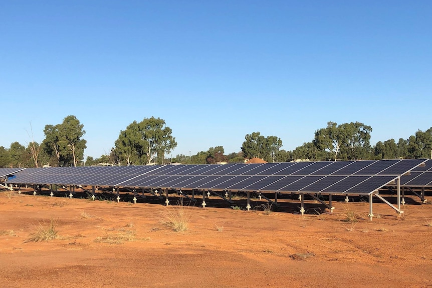 Flat ground-mounted solar panels on red brown dirt.