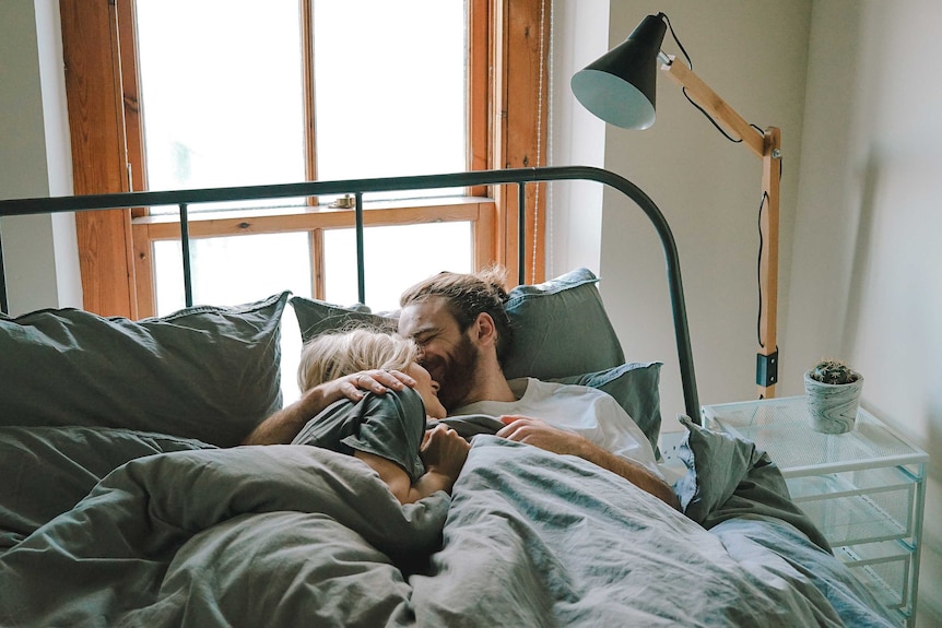 Man and woman cuddle in bed to depict information on how to switch up predictable, routine sex.