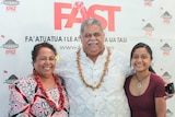 Two women and a man stand arm in arm and smile as they pose for a photo in front of a political party logo reading FAST