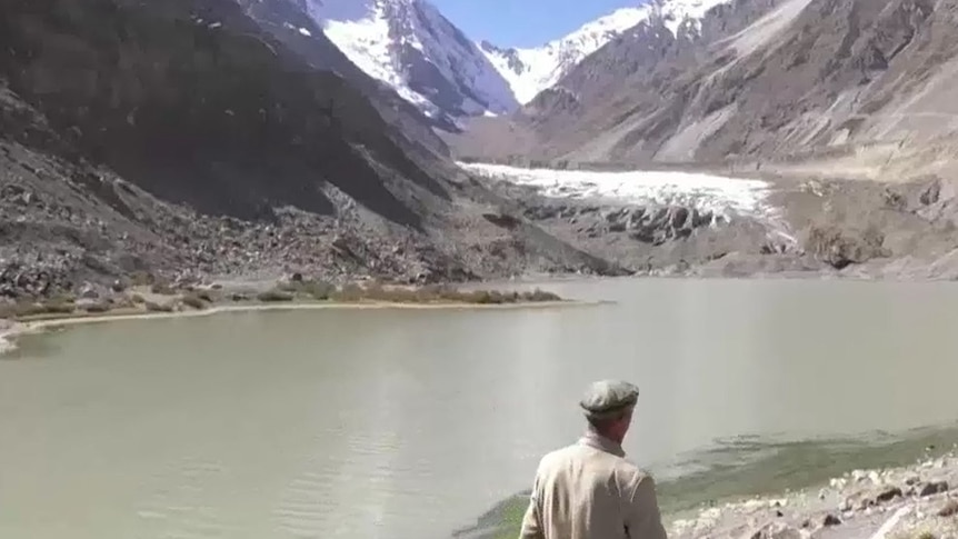 Man walking next to a lake created by melting glaciers, glacier behind the lake.