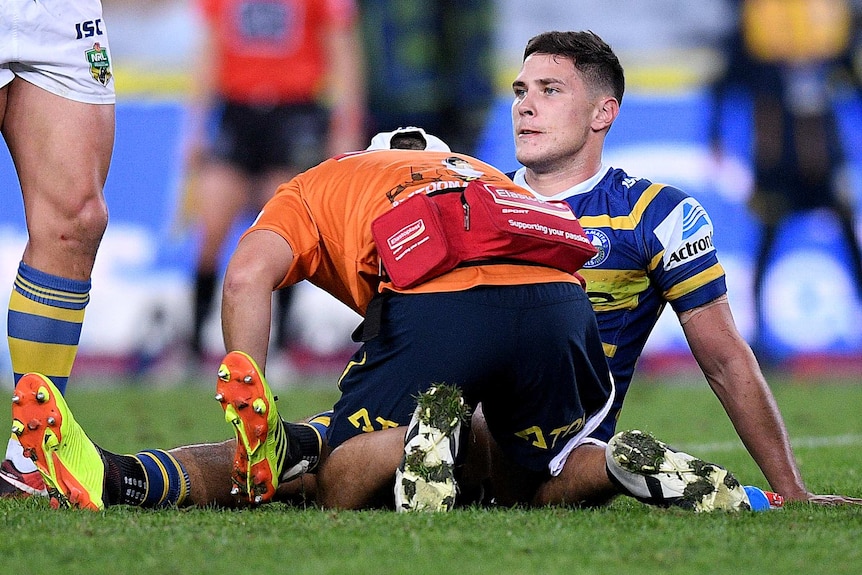 Rugby League trainer tending to an injured player who is sitting down on the field during a game