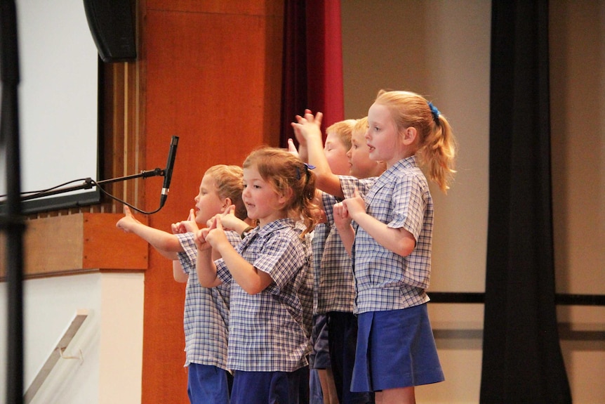 A group of children recite a poem in front of a microphone.