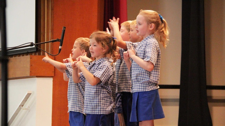 A group of children recite a poem in front of a microphone.