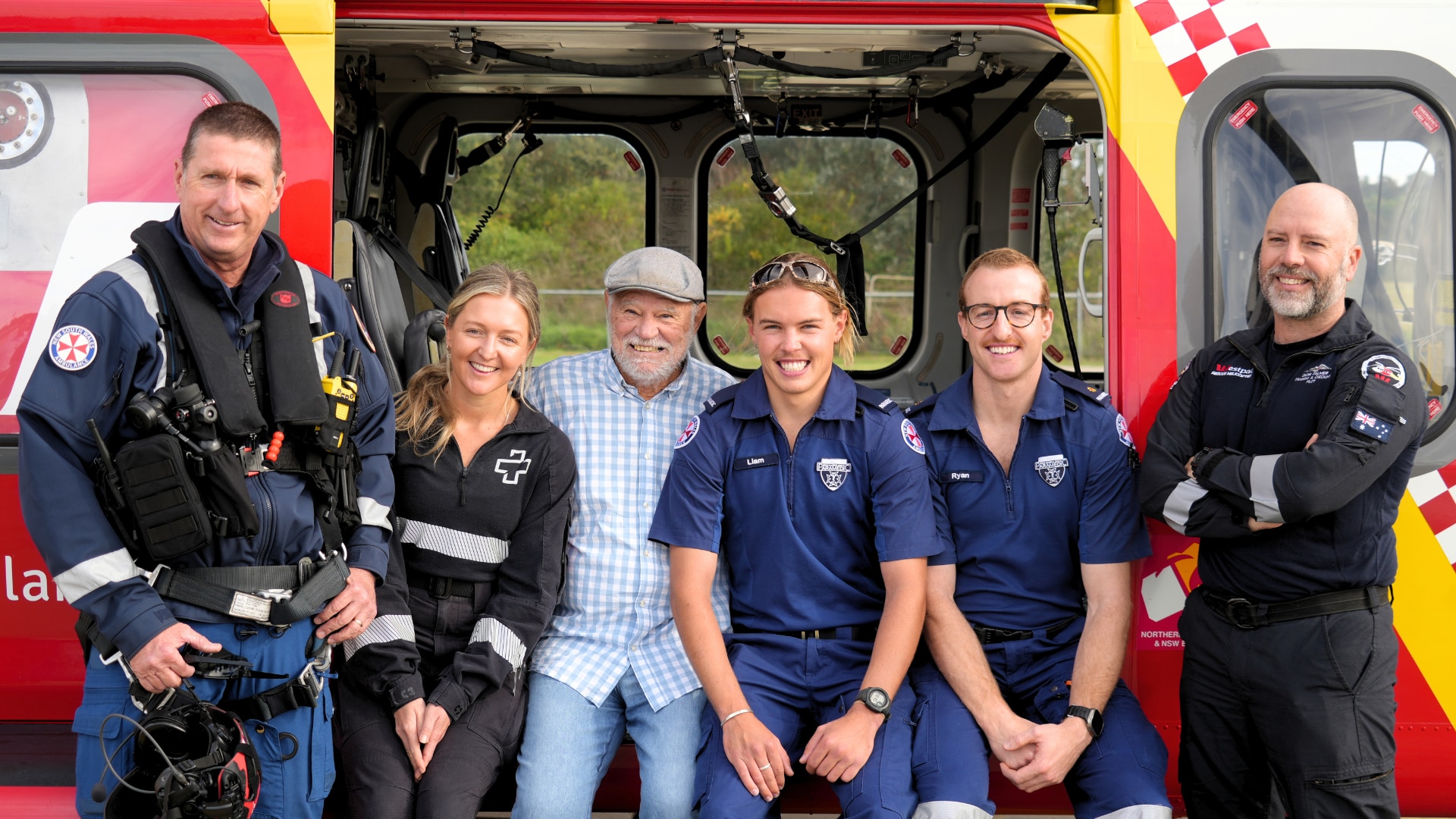 An elderly man sitting on the edge of a rescue helicopter, flanked by paramedics and doctors on either side.