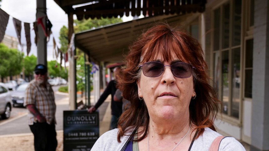 A woman with dark red hair and purple glasses stands in the main street of Dunolly.