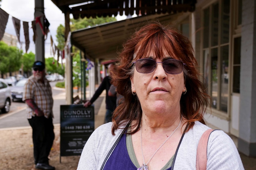 A woman with dark red hair and purple glasses stands in the main street of Dunolly.