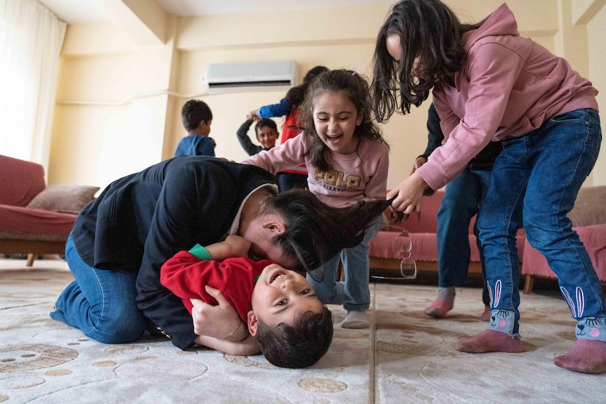 A group of Turkish and Syrian children play together on the ground.