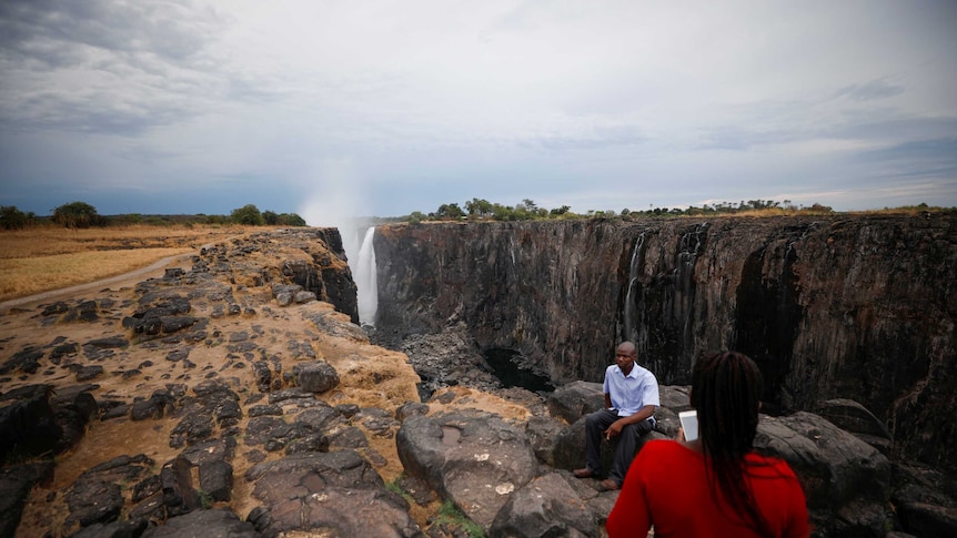 Visitors take pictures before dry cliffs following a prolonged drought at Victoria Falls.