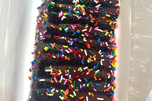 A large slice of chocolate cake covered in coloured sprinkles.