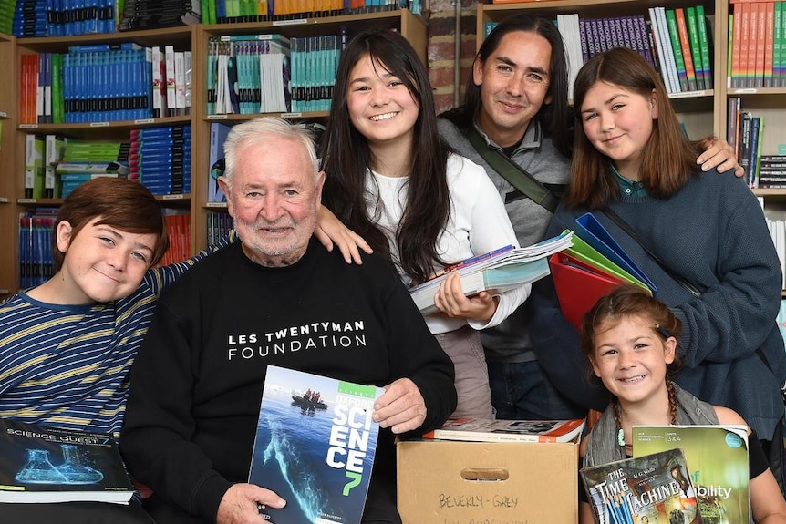 Les and a group of children holding books. 