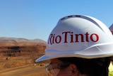 Rio Tinto worker, wearing a hard hat, looks out at a mine site.