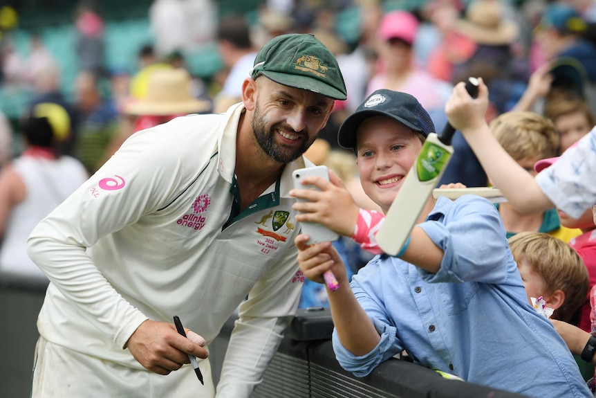 A smiling Australian player stands next to a young cricket fan near the boundary after a Test.