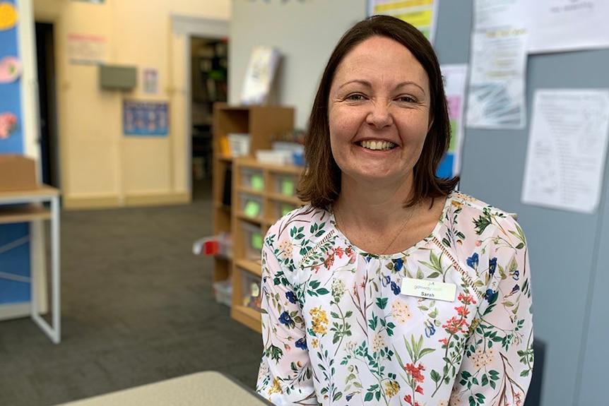 Woman sits behind desk in a primary school classroom