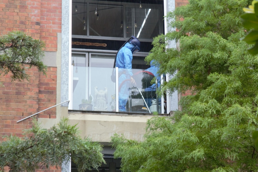 Man in a blue hazmat suit and respirator vacuuming on an apartment balcony