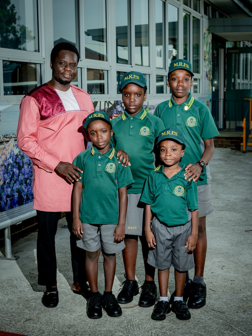 Victor smiles in a portrait with his four children, who are wearing green school shirts.