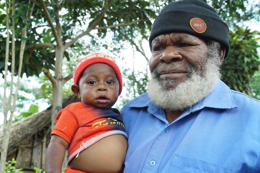 A father wearing a beanie holds his son in his arms