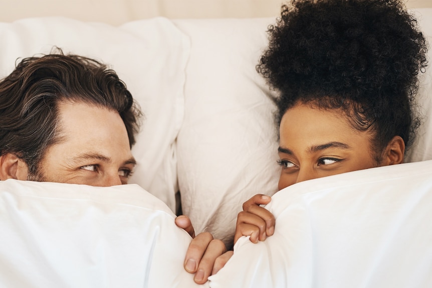 man and woman looking at each other in bed with covers pulled up