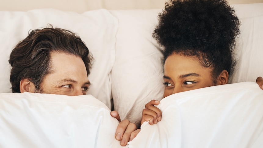 man and woman looking at each other in bed with covers pulled up