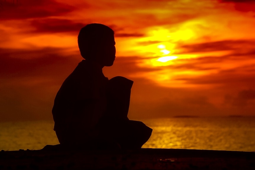 Silhouette of boy watching spectacular red sunset.
