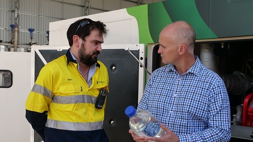 Two men in high vis and work shirts speaking to each other inside a large warehouse.