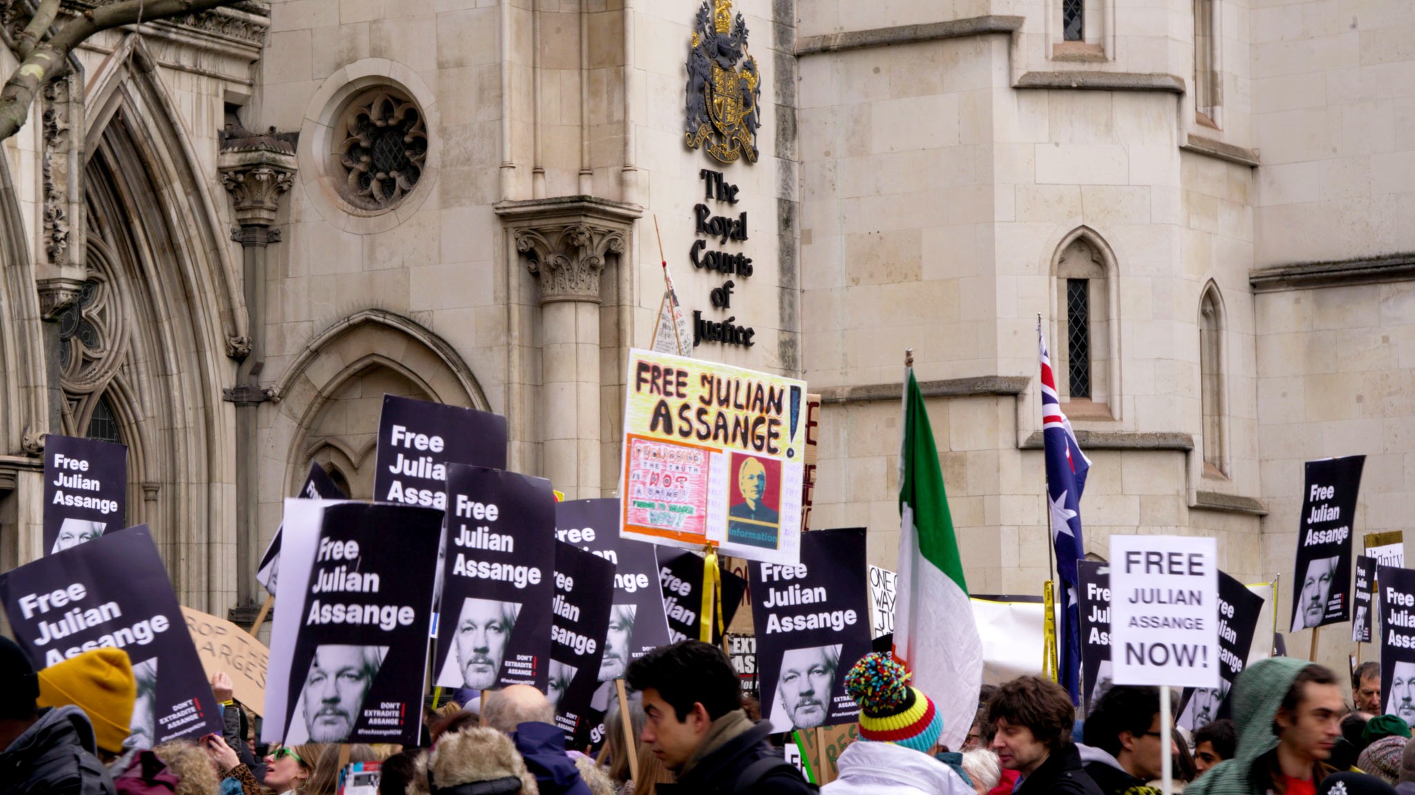 A large crowd of people holding signs with supportive slogans of Julian Assange