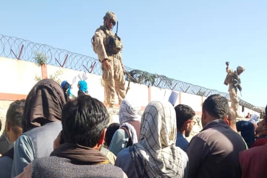 A soldiers stands on a wall at Kabul airport as people reach out to him.