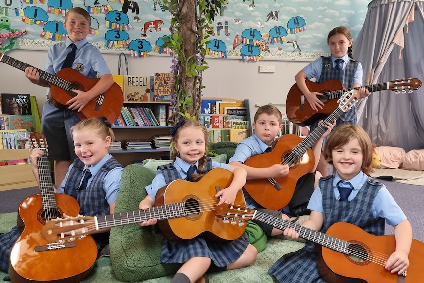 Six students with guitars sitting under a fake tree in a classroom