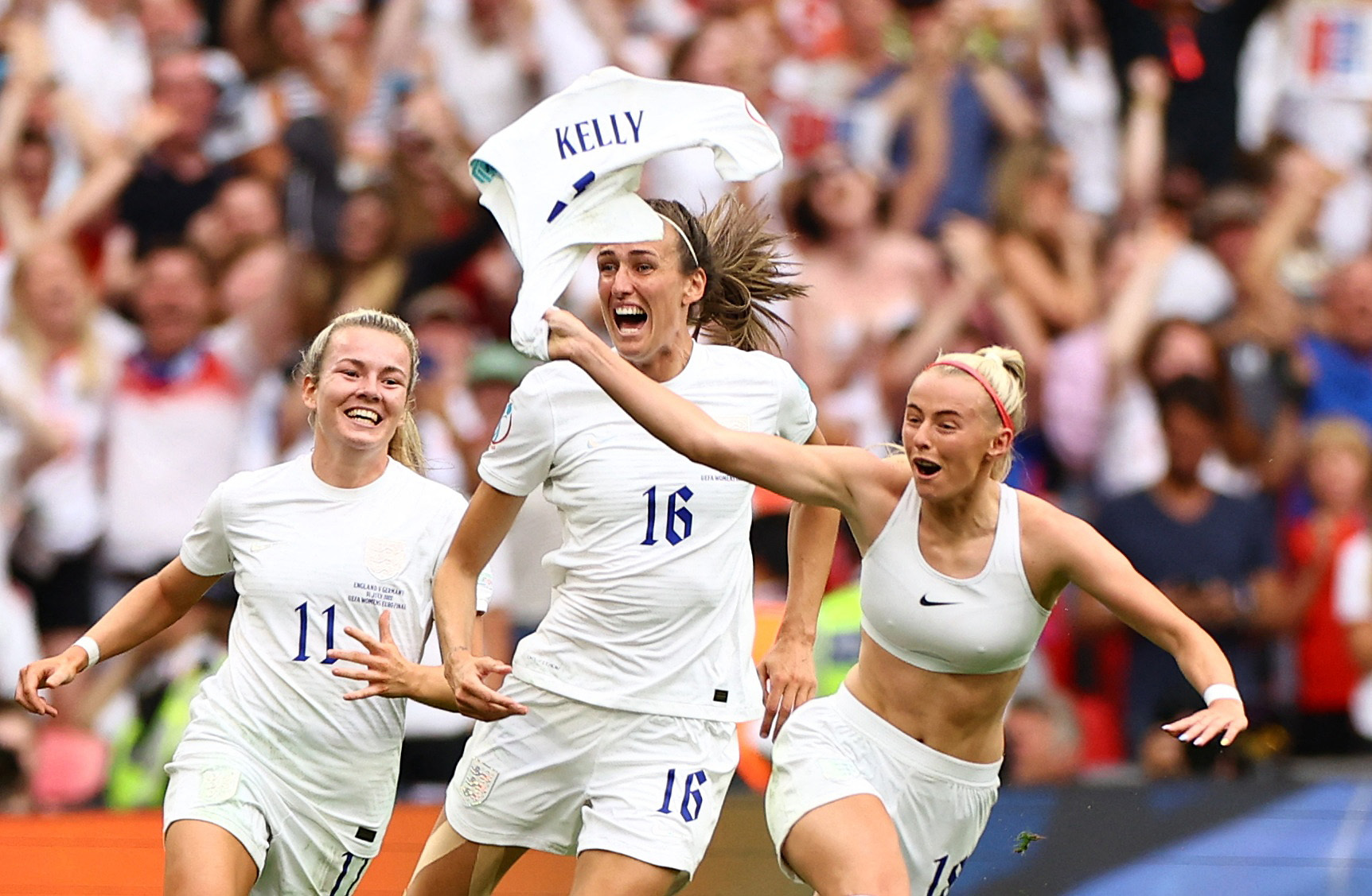 三名女足球员正喜气洋洋地跑过足球场庆祝胜利。一群人在他们身后。 
