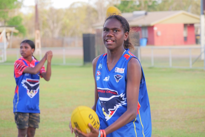 A woman smiles at the camera as she handballs a footy