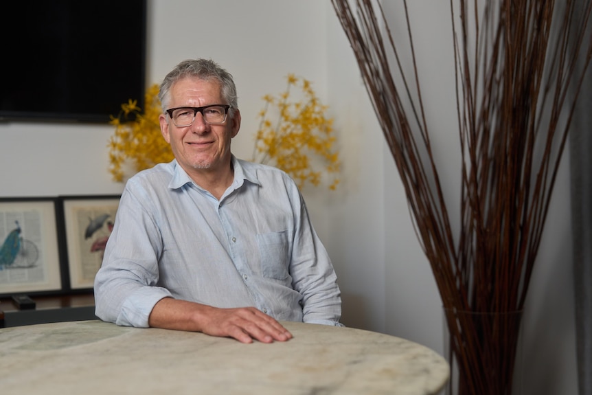 portrait shot of Gordon Renouf sitting at table with yellow flowers in background