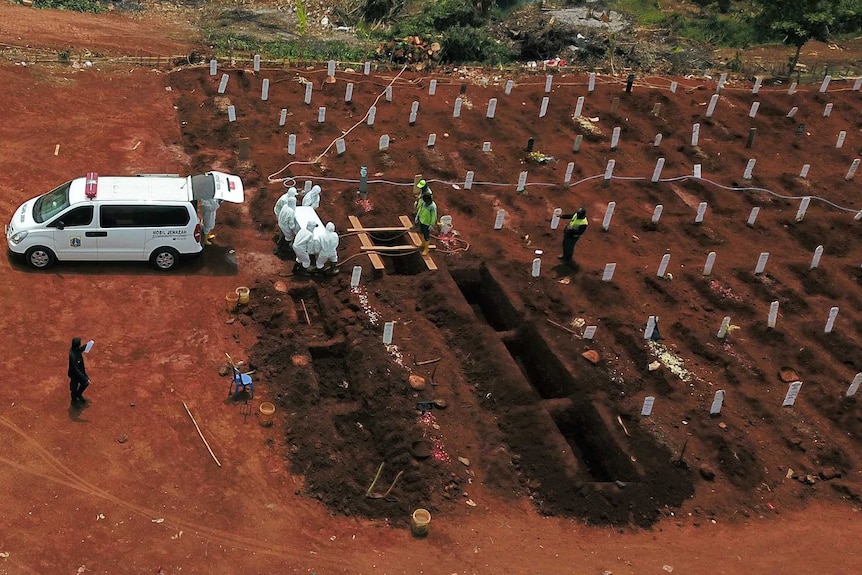 A group of people wearing protective clothing bury a coffin.