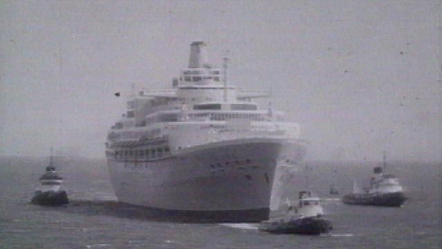 Large ocean liner at sea surrounded by tug boats