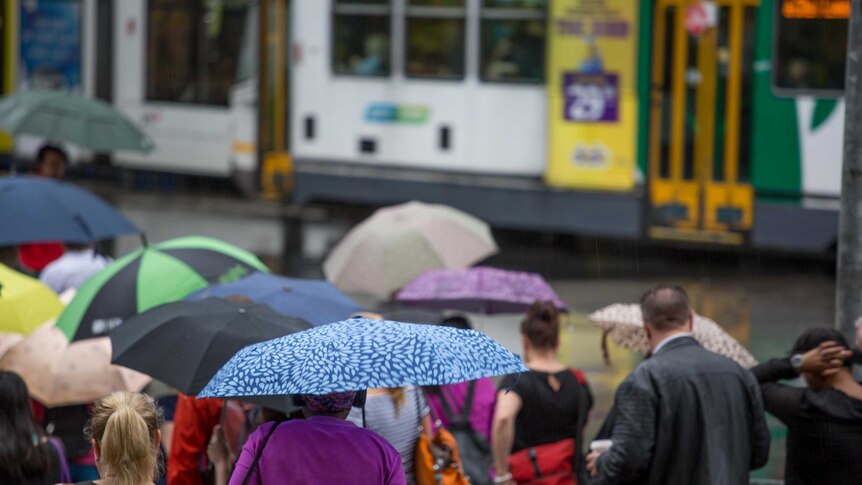 Pedestrians cross the road at Flinders Street, as rain pours down.