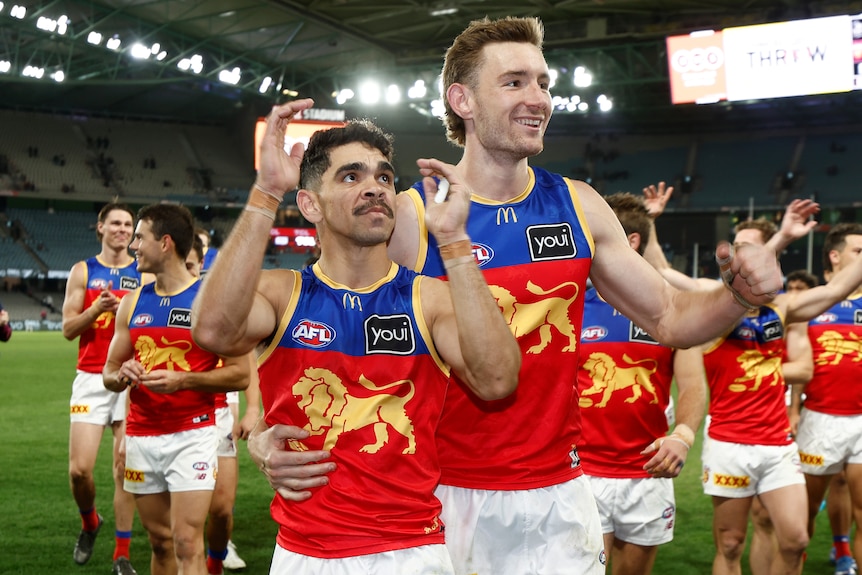 Two Brisbane Lions AFL players applaud the fans as they look up into the stands after a game.