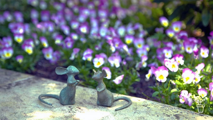 Two mouse statues sitting on edge of flower bed in a garden