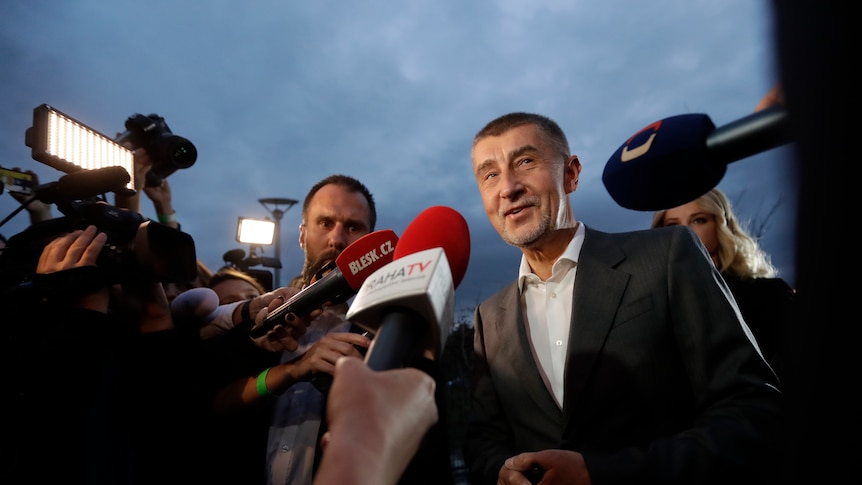 Andrej Babis speaks to media with microphones in his face.