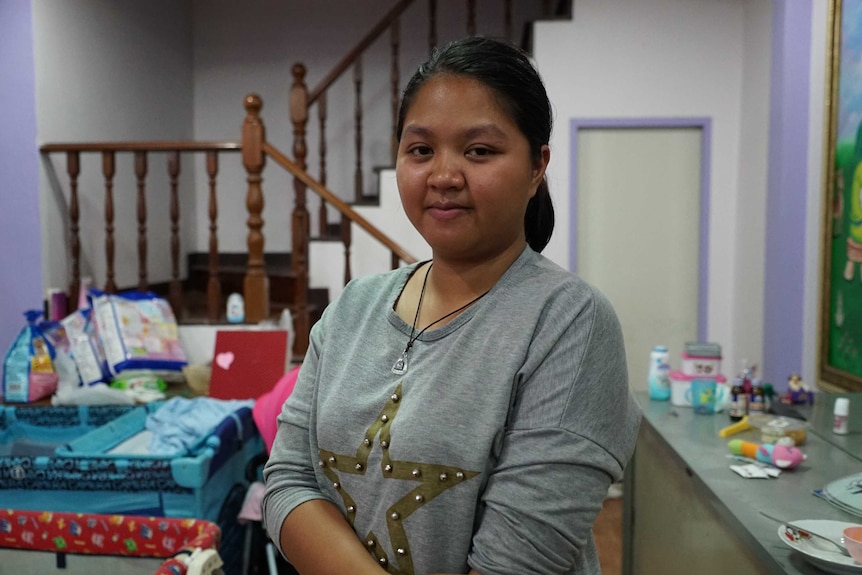 Goy wears a grey shirt with a gold studded star emblem on the front and looks at the camera with a slight smile.