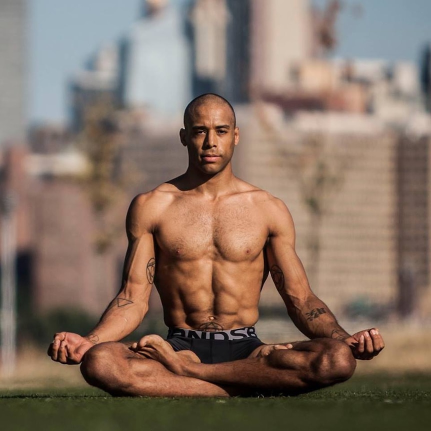 A mid-shot of Raoul Kawusu Conteh Smith shirtless and sitting in the lotus position in a park.