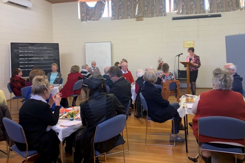 A crowd of people sit down at tables spread out across a room